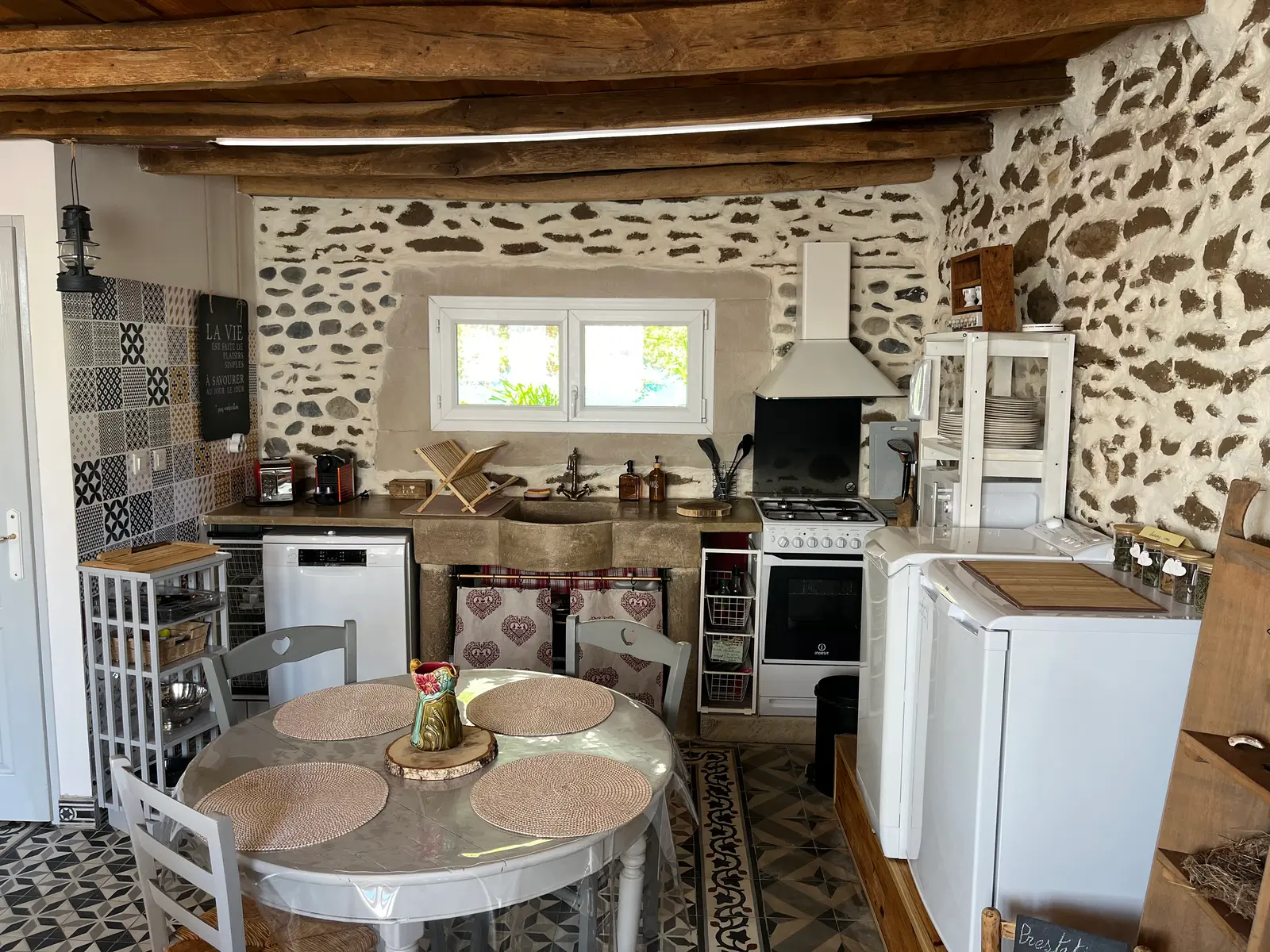 Le coin cuisine du gîte : évier en pierre ancienne, gazinière, lave-vaisselle, mur en galets.