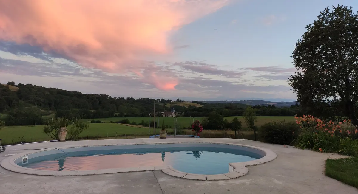 La piscine du gîte au coucher du soleil, nuages roses, les collines béarnaises et les Pyrénées à l’horizon.